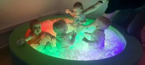 Dzieci bawią się piłeczkami w kolorowym, świecącym baseniku.