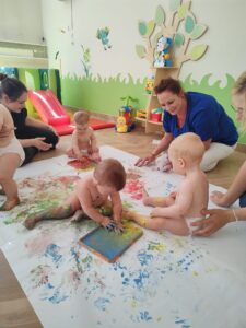 Opiekunka maluje z dziećmi farbami.