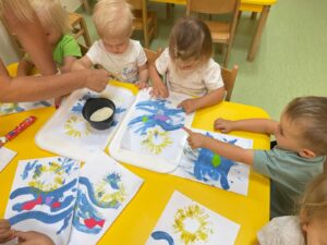 Dzieci posypują kartkę kaszą manną, tworząc plażę