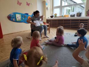 Czytanie dzieciom siedzącym na dywanie przez Panią bibliotekarkę.