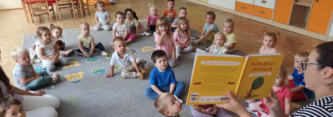 Czytanie dzieciom siedzącym na dywanie przez Panią bibliotekarkę.