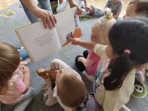 Czytanie dzieciom siedzącym na dywanie przez Panią bibliotekarkę.