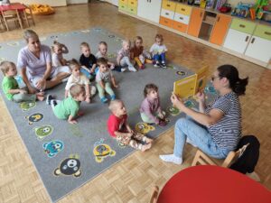 Czytanie dzieciom siedzącym na dywanie przez Panią bibliotekarkę.