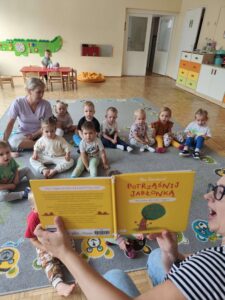 Czytanie dzieciom siedzącym na dywanie przez Panią bibliotekarkę.