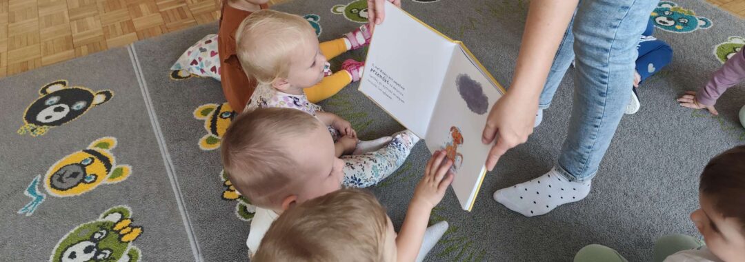 Czytanie dzieciom siedzącym na dywanie przez Panią bibliotekarkę.