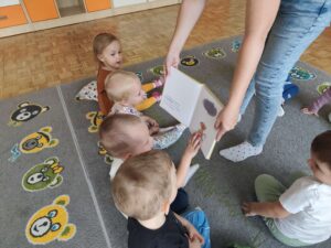 Czytanie dzieciom siedzącym na dywanie przez Panią bibliotekarkę.
