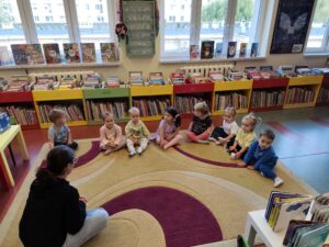 Pani w bibliotece czyta dzieciom książkę siedząc na dywanie