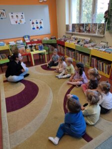 Pani w bibliotece czyta dzieciom książkę siedząc na dywanie