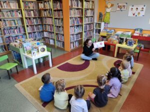 Pani w bibliotece czyta dzieciom książkę siedząc na dywanie