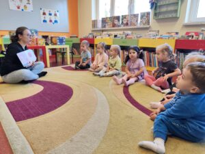 Pani w bibliotece czyta dzieciom książkę siedząc na dywanie