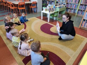 Pani w bibliotece czyta dzieciom książkę siedząc na dywanie
