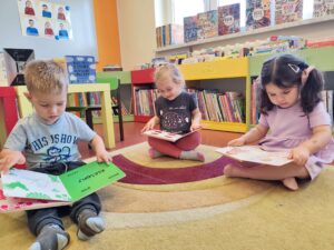 Dzieci siedzą na dywanie w bibliotece i oglądają książeczki