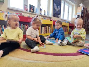 Dzieci siedzą na dywanie w bibliotece i oglądają książeczki