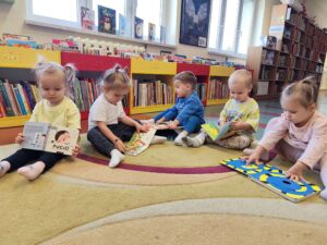 Dzieci siedzą na dywanie w bibliotece i oglądają książeczki