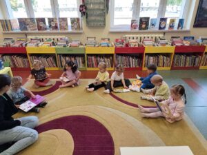 Dzieci siedzą na dywanie w bibliotece i oglądają książeczki