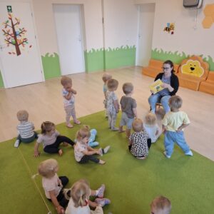 Czytanie dzieciom siedzącym na dywanie przez Panią bibliotekarkę.