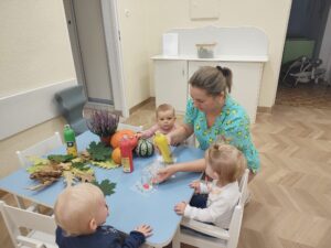 Ciocia rozdaje dzieciom woreczki z farbą. Dzieci będą malować liście farbami.