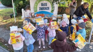 Dzieci na podwórku trzymają w górze paczki z chrupkami