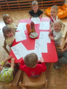 Dzieci siedzą przy stoliku przed wykonaniem pracy plastycznej