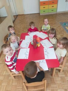 Dzieci siedzą przy stoliku przed wykonaniem pracy plastycznej