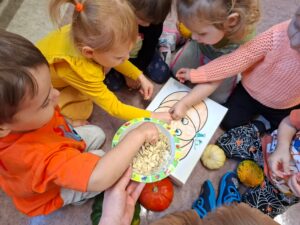 Dzieci wkładają pestki do pudełka z namalowaną dynią