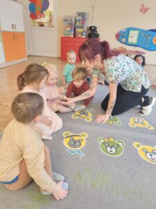 Dzieci siedzą na dywanie a opiekunka pokazuje im kasztany