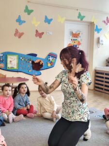 Dzieci siedzą na dywanie a opiekunka pokazuje im liście