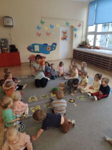Dzieci siedzą na dywanie a opiekunka pokazuje im pluszową wiewiórkę