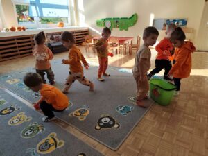 Dzieci zbierają pomarańczowe piłeczki z dywanu i wrzucają je do wiaderka