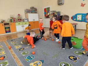 Dzieci zbierają pomarańczowe piłeczki z dywanu i wrzucają je do wiaderka