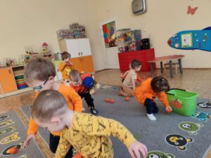 Dzieci zbierają pomarańczowe piłeczki z dywanu i wrzucają je do wiaderka