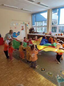 Dzieci machają chustą animacyjną na której znajdują się pomarańczowe piłeczki