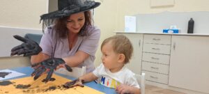Ciocia pomaga odbić rączkę na kartce papieru.