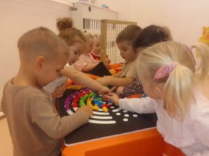 Dzieci układają tęczę z kolorowych ksztatków na stole sensorycznym