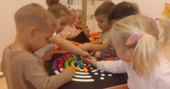 Dzieci układają tęczę z kolorowych ksztatków na stole sensorycznym