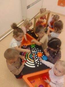 Dzieci układają tęczę z kolorowych ksztatków na stole sensorycznym