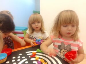 Dzieci układają tęczę z kolorowych ksztatków na stole sensorycznym