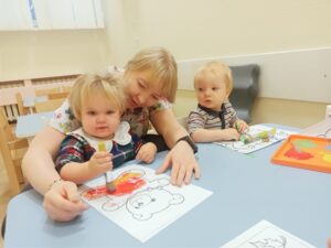 Dziewczynka maluje misia farbą. ciocia jej pomaga.