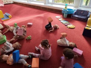 Dzieci leżą na dywanie i próbują utrzymać stopami piankowe kostki