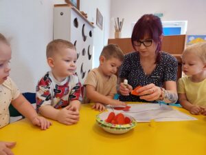 Dzieci wraz z opiekunem przyklejają czerwone serca na flagę Polski