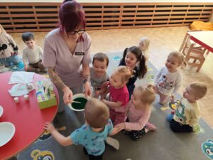 Opiekunka pokazuje dzieciom technikę mieszania kolorów przy pomocy barwników spożywczych
