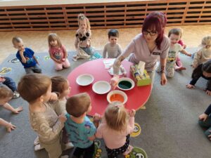 Opiekunka pokazuje dzieciom technikę mieszania kolorów przy pomocy barwników spożywczych