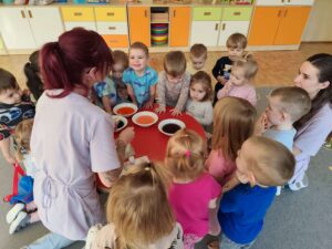 Opiekunka pokazuje dzieciom technikę mieszania kolorów przy pomocy barwników spożywczych