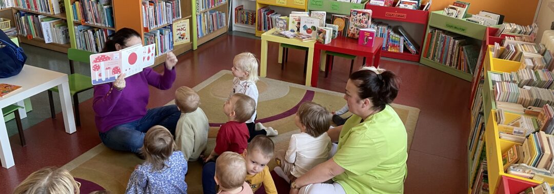 Pani z biblioteki pokazuje i czyta dzieciom książeczkę