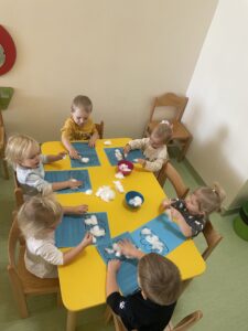 Dzieci przyklejają na kontur chmurki watę oraz odbijają paluszkiem zamoczonym w białej farbie kropelki deszczu