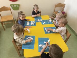 Dzieci przyklejają na kontur chmurki watę oraz odbijają paluszkiem zamoczonym w białej farbie kropelki deszczu