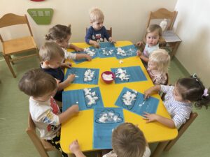Dzieci przyklejają na kontur chmurki watę oraz odbijają paluszkiem zamoczonym w białej farbie kropelki deszczu