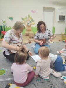 Dzieci z opiekunkami w trakcie zajęć z wykorzystaniem instrumentu ukulele.