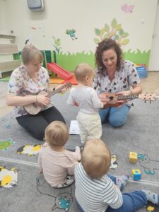 Dzieci z opiekunkami w trakcie zajęć z wykorzystaniem instrumentu ukulele.