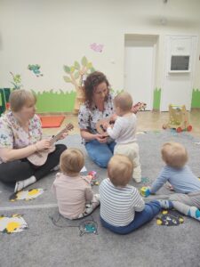 Dzieci z opiekunkami w trakcie zajęć z wykorzystaniem instrumentu ukulele.